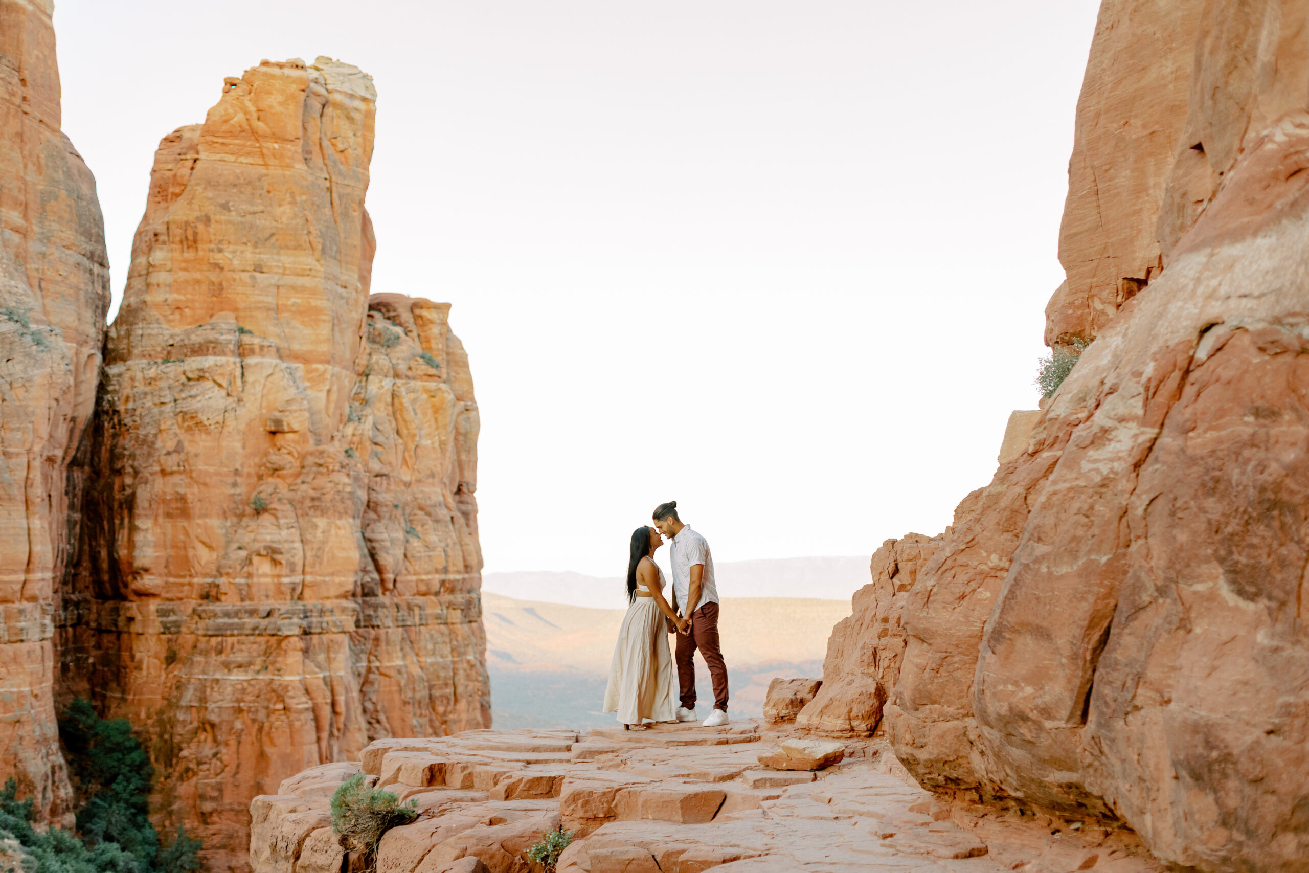 Photo of Lakin and Jasmyne at Sunrise:
"Lakin and Jasmyne stand together on top of Cathedral Rock in Sedona at sunrise, with the warm, golden light highlighting their joyful expressions and the stunning red rock formations in the background."