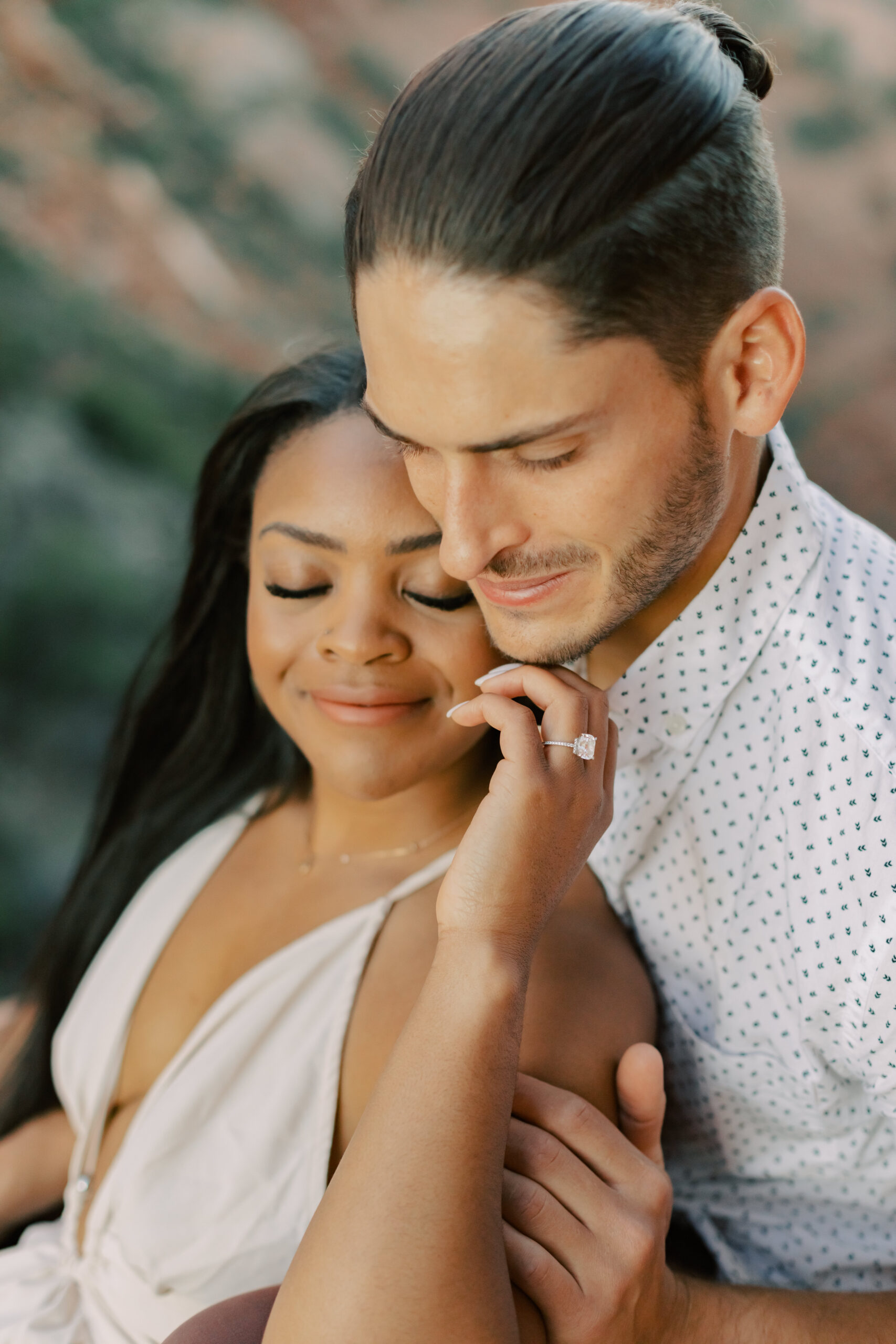 Photo of Engagement Rings in Sedona:
"A close-up of Jasmyne's hand resting on Lakin's chin, showing off their engagement rings with the rugged and beautiful Sedona terrain as the backdrop."