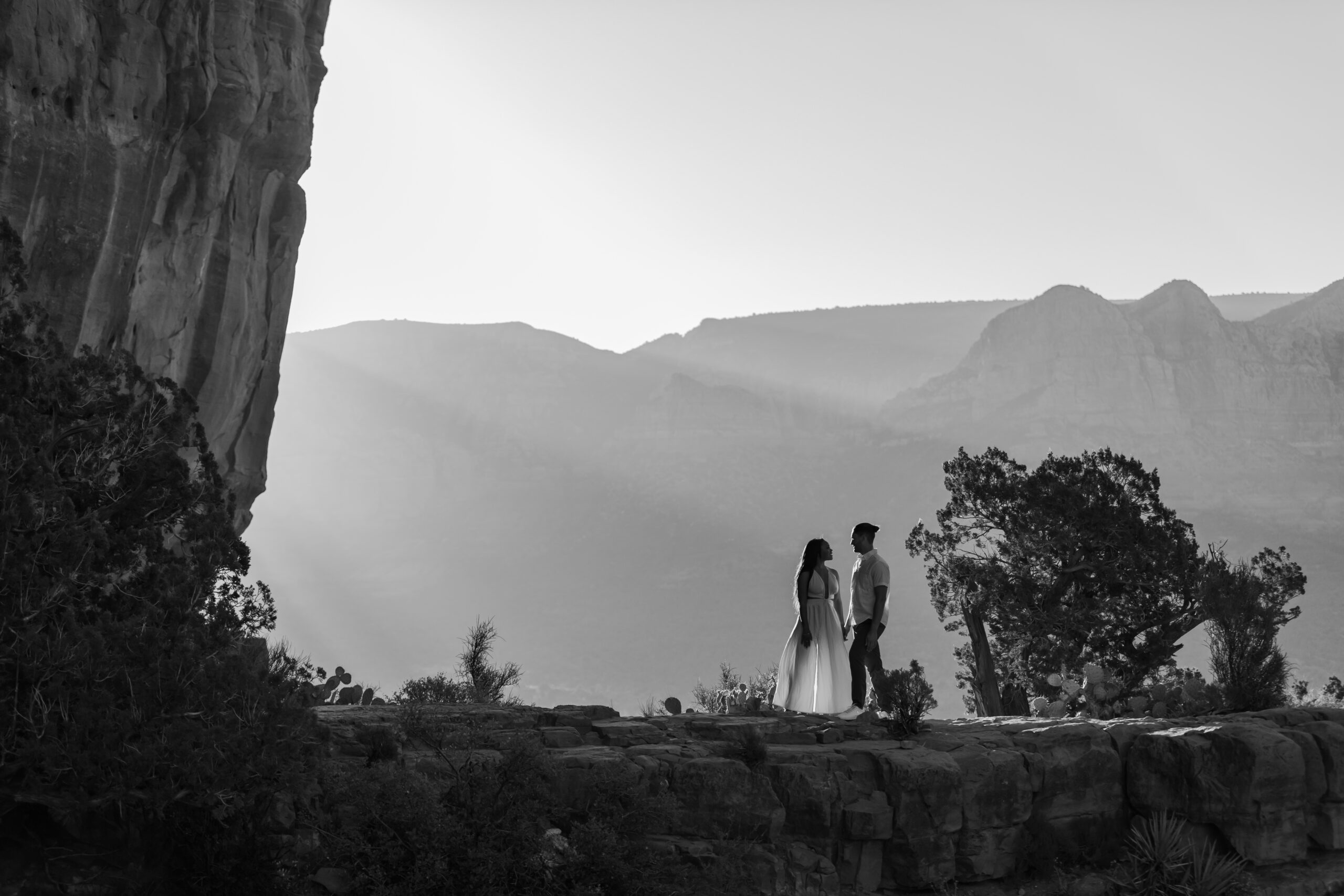 Black and white wide Shot of Lakin and Jasmyne on Cathedral Rock:
"A wide shot of Lakin and Jasmyne standing on the edge of Cathedral Rock, holding hands and gazing into the distance, with the vast and colorful Sedona landscape stretching out below them."