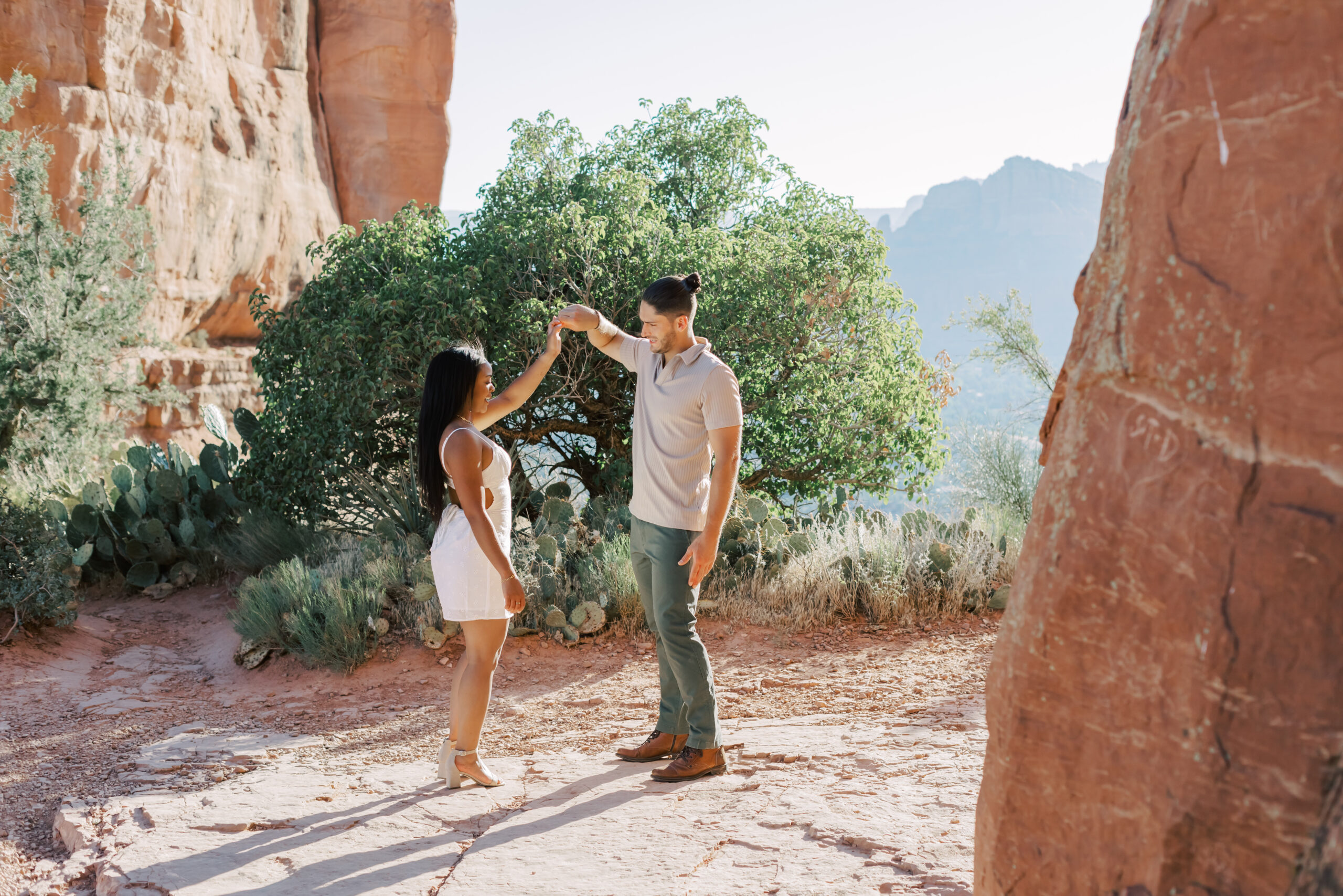 Photo of Lakin and Jasmyne at Sunrise:
"Lakin and Jasmyne stand together on top of Cathedral Rock in Sedona at sunrise, with the warm, golden light highlighting their joyful expressions and the stunning red rock formations in the background."