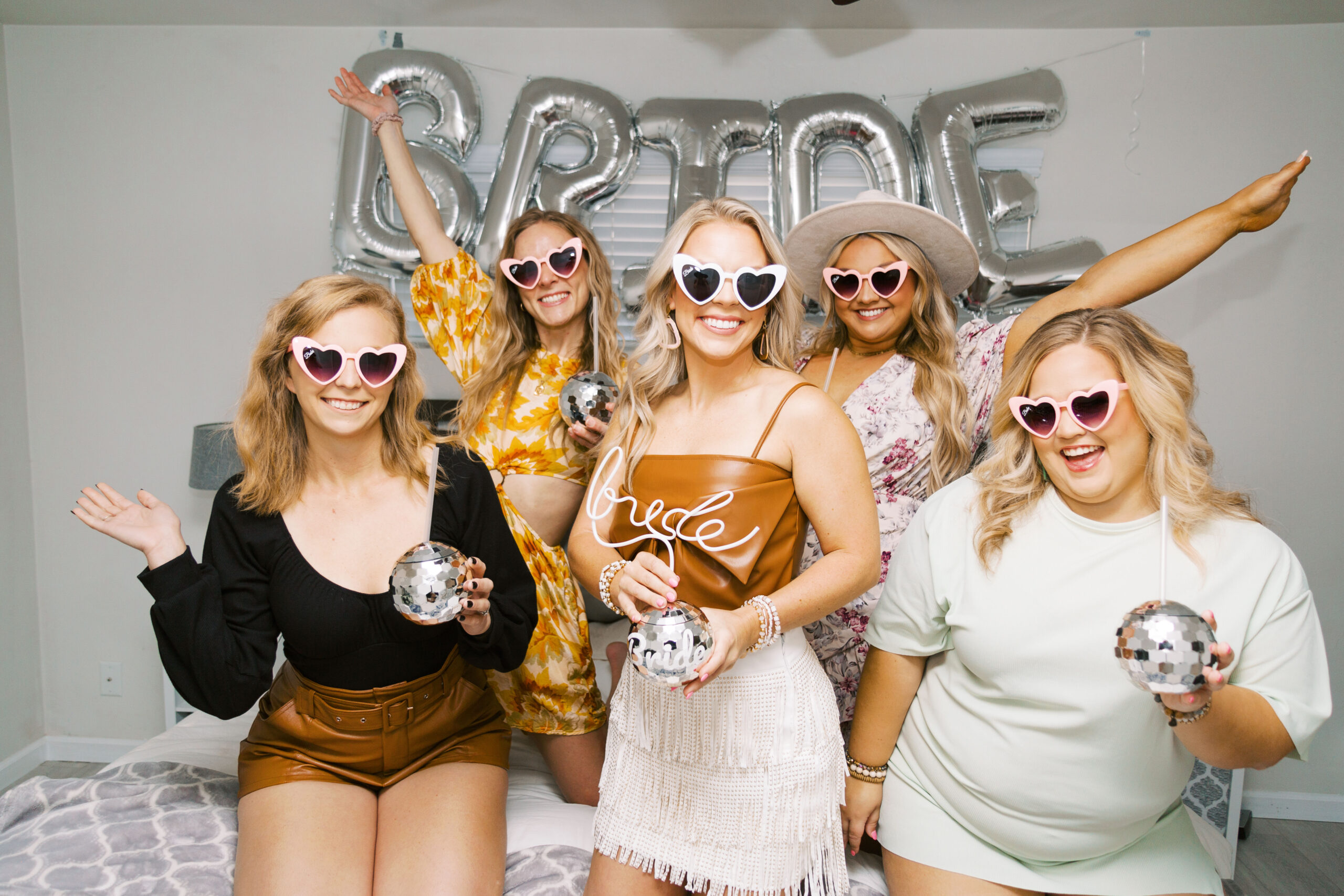 Bride-to-be holding a fun bachelorette party drink in a disco cup with friends gathered around smiling and laughing while celebrating in Scottsdale, Arizona.